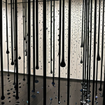 **Prompt:** A darkened room at MoMA, NYC. Droplets of water rhythmically falling on metallic chimes. Cool mist, play of light. Transformative experience.